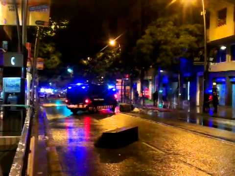 Des d·un balcó del C/ de Sants sona L·Estaca de Lluis Llach mentre passen els antidisturbis dels mossos amunt i avall i la gent al carrer i als balcons pica cassoles.
